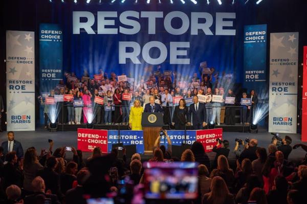 Joe Biden, Kamala Harris on stage at a rally under a sign saying 'Restore Roe'.